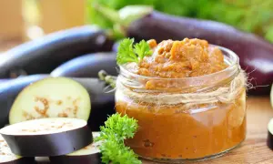 Un pot de caviar d'aubergine, garni de persil frais, entouré d'aubergines entières et tranchées.