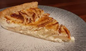 Une part de tarte aux pommes à l'ancienne, avec sa garniture crémeuse et ses pommes caramélisées, sur une assiette décorée.