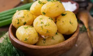 Pommes de terre à l'eau, tendres et parsemées d'aneth frais, dans un bol en bois. Un plat simple et savoureux.