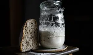 Une tranche de pain au levain maison à côté d'un bocal rempli de levain actif.