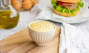 Sauce burger maison crémeuse, garnie de flocons, prête à accompagner un burger savoureux. Huile d'olive et œufs en arrière-plan.