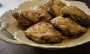 Plusieurs hauts de cuisse de poulet au four, dorés et assaisonnés d'herbes, reposent sur une assiette blanche festonnée.