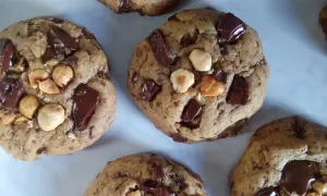 Gros plan sur des cookies américains faits maison, débordant de pépites de chocolat noir et de noisettes. Parfaits pour une recette de cookies américain gourmande.
