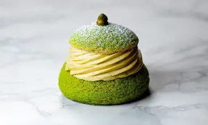 Un Paris Brest pistache, un délice vert et doré, saupoudré de sucre glace, sur fond marbré.