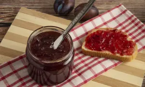 Un pot de confitures de quetsches maison, une tartine généreusement garnie et quelques quetsches sur une planche en bois.