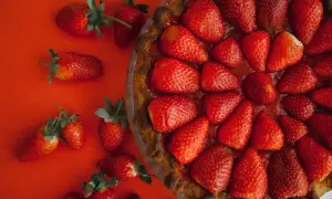 Tarte aux fraises sans crème pâtissière, garnie de fruits rouges frais sur fond rouge. Un délice simple et fruité.