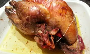 Une pintade au four, dorée et juteuse, repose dans un plat blanc, baignant dans son jus savoureux.