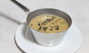 Sauce au poivre recette de chef, onctueuse et garnie de grains de poivre concassés, servie dans une petite casserole en métal sur une assiette blanche.