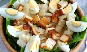 Salade César appétissante dans un bol en bois, garnie d'œufs durs, de croûtons dorés et d'une onctueuse sauce César.