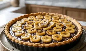 Délicieuse tarte banane chocolat, garnie de rondelles de banane caramélisées et de copeaux de chocolat noir. Un régal pour les yeux et les papilles.