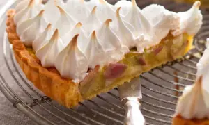 Une part de tarte rhubarbe meringuée, avec sa croûte dorée et sa garniture acidulée, surmontée d'une meringue légère et aérienne.