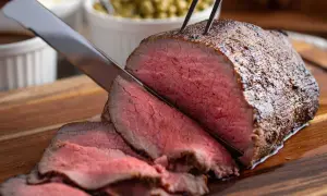 Un délicieux rôti de boeuf, coupé en fines tranches rosées, est prêt à être servi avec des accompagnements.