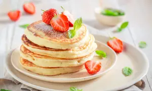Pile de pancakes moelleux, parsemés de sucre glace et ornés de fraises fraîches et de menthe. Un délice digne des pancakes Cyril Lignac.