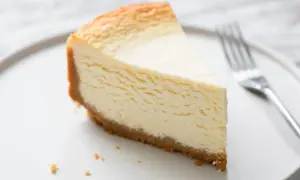Une part de gâteau au fromage blanc onctueux, digne d'un gâteau au fromage blanc Cyril Lignac, sur une assiette blanche avec une fourchette.