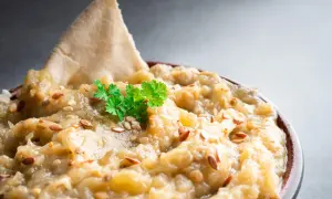 Un bol de le vrai caviar d'aubergine, garni de persil frais et de graines de sésame, avec un morceau de pain pita.