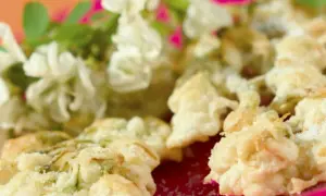 Délicieux beignets de fleur d'acacia à la poêle, saupoudrés de sucre, avec des fleurs fraîches en arrière-plan.