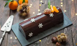 Bûche marron glacé, décorée de flocons et de quartiers de clémentine, évoquant la magie de Noël.