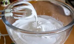 Fouets de batteur électrique en train de battre les blancs en neige dans un bol en verre, créant une texture aérienne parfaite pour une meringue.