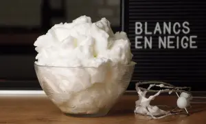 Un bol de blancs en neige aériens, comme un nuage, à côté d'un batteur. Le mot "BLANCS EN NEIGE" est visible sur un panneau.