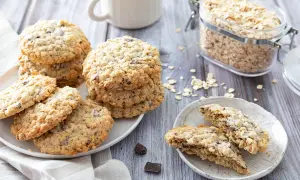 Des biscuits flocons d'avoine aux pépites de chocolat, empilés sur une assiette, avec un bocal de flocons d'avoine en arrière-plan.