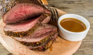 Un délicieux roti de boeuf basse température, tranché et servi avec une sauce savoureuse sur une planche en bois.