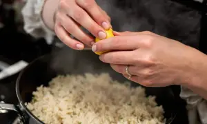 Cuisson du riz rouge : une main presse un quartier de citron sur le riz fumant dans une casserole.