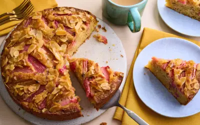 Un délicieux dessert rhubarbe gastronomique, un gâteau aux amandes effilées et à la rhubarbe rose, servi sur une assiette bleue.