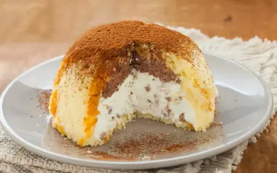 Gâteau glacé en forme de dôme, garni de crème et de chocolat, saupoudré de cacao. Parfait pour une recette génoise.