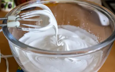 Fouets de batteur électrique en train de battre les blancs en neige dans un bol en verre, créant une texture aérienne parfaite pour une meringue.