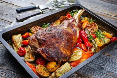 Un plat appétissant d'épaule d'agneau au four, rôti à la perfection avec des légumes colorés comme des poivrons, des tomates et de l'ail.