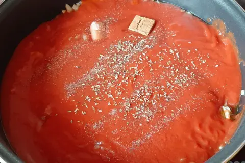 Sauce tomate maison mijote dans une poêle, agrémentée d'herbes et d'un cube de bouillon.