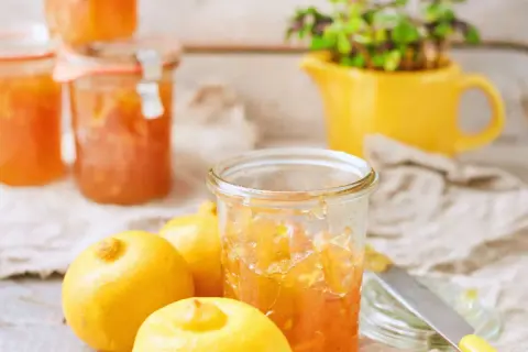 Bocaux de marmelade de citron italienne, avec des citrons frais et une plante verte dans un pichet jaune en arrière-plan.