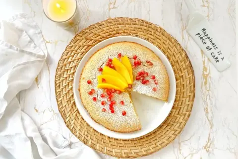 Un délicieux flan coco saupoudré de sucre glace, garni de mangue et de grenades. Une part manque, invitant à la gourmandise.