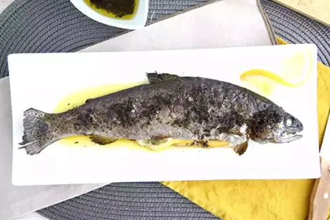 Une truite au four entière, dorée et savoureuse, servie sur une assiette blanche avec des quartiers de citron. Un délice simple et sain.