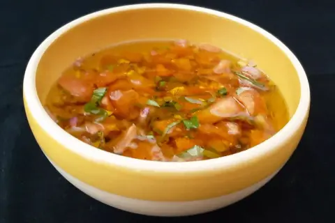Un bol jaune contient une sauce vierge fraîche, avec des dés de tomates, des herbes vertes et une vinaigrette translucide.