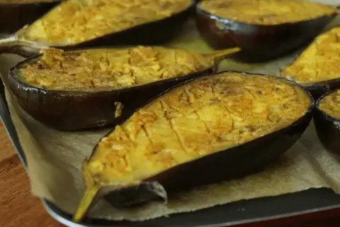 Aubergines au four, coupées en deux et garnies d'une préparation dorée, prêtes à être dégustées.
