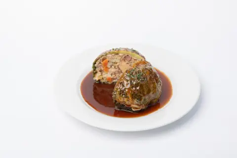 Chou farci, une recette du carnet de Julie, servi avec une sauce brune et garni d'herbes.
