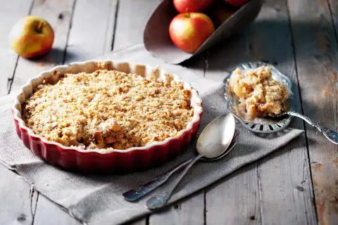 Un délicieux crumble pomme tout juste sorti du four, servi dans un plat rouge, avec une portion sur une cuillère ornée.