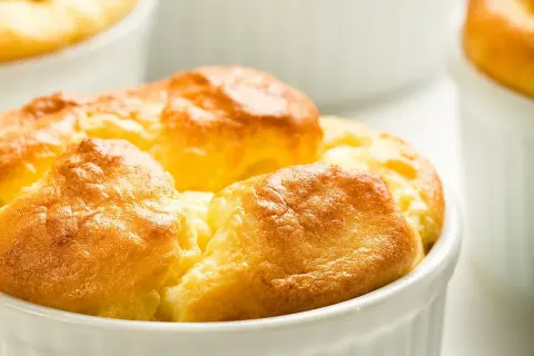 Soufflés au fromage dorés et gonflés dans leurs ramequins, prêts à être dégustés. Une recette simple pour un plat aérien.