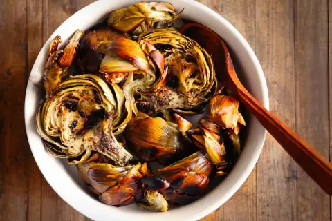 Artichauts barigoule à la façon Etchebest, rôtis et caramélisés, servis dans un plat blanc avec une cuillère en bois.