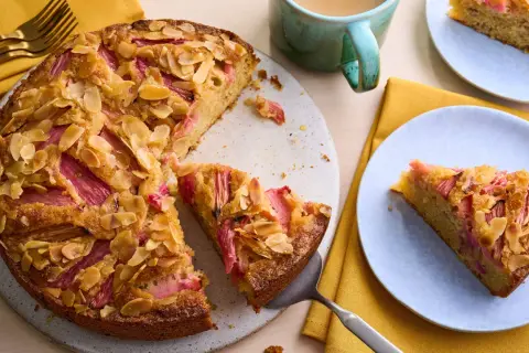 Un délicieux dessert rhubarbe gastronomique, un gâteau aux amandes effilées et à la rhubarbe rose, servi sur une assiette bleue.