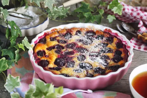 Un délicieux clafoutis aux prunes, saupoudré de sucre glace, prêt à être dégusté avec une tasse de thé.