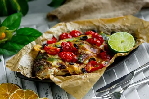 Dorade en papillote, savoureuse et colorée, garnie de tomates cerises, d'olives et d'une tranche de citron vert.