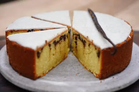 Gâteau poudre d'amande facile et rapide, avec glaçage blanc et éclats de chocolat. Une gousse de vanille décore ce délice.
