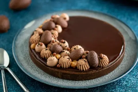Délicieuse tarte chocolat caramel, ornée d'œufs en chocolat et de touches de crème, prête à être dégustée.
