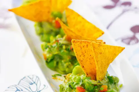 Guacamole maison, une recette facile et savoureuse. Des chips tortilla plongent dans ce délice vert.