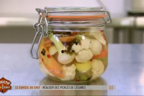Un bocal de pickles de légumes colorés, comme ceux préparés par un Top Chef, rempli de chou-fleur, carottes et oignons.