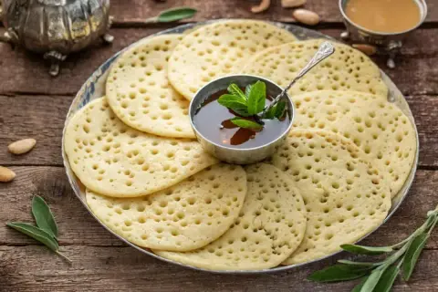 Une assiette de crêpes mille trous, garnie d'une coupelle de miel et de menthe fraîche, prête à être dégustée.