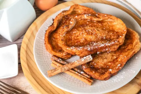 Trois tranches de pain perdu dorées, saupoudrées de sucre glace et garnies de bâtons de cannelle. Un délice pour le petit-déjeuner.