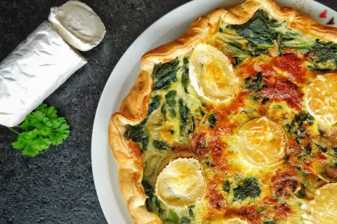Tarte épinard chèvre dorée, avec du fromage de chèvre frais à côté et une touche de persil.